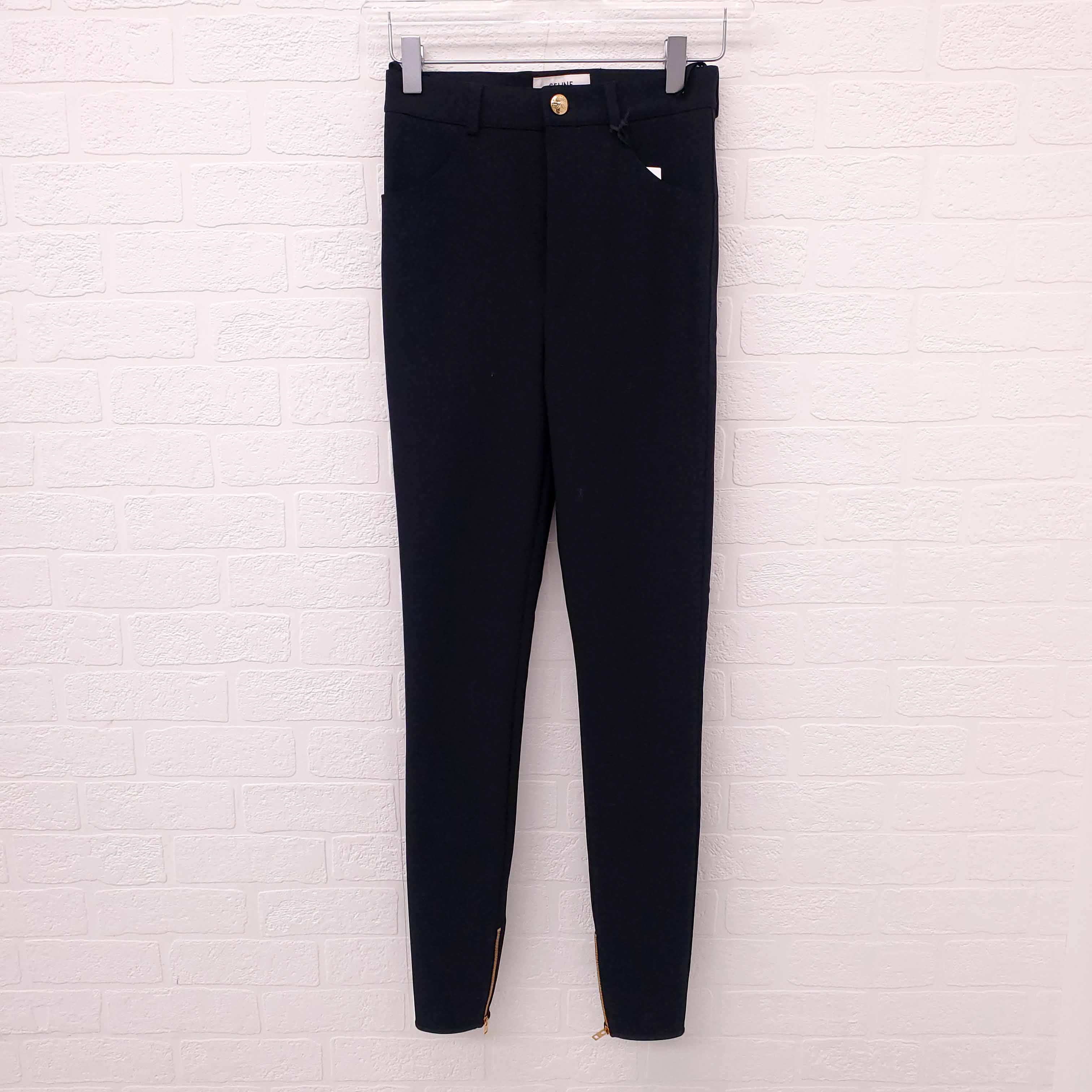 Black Celine pants hanging on a white brick wall.