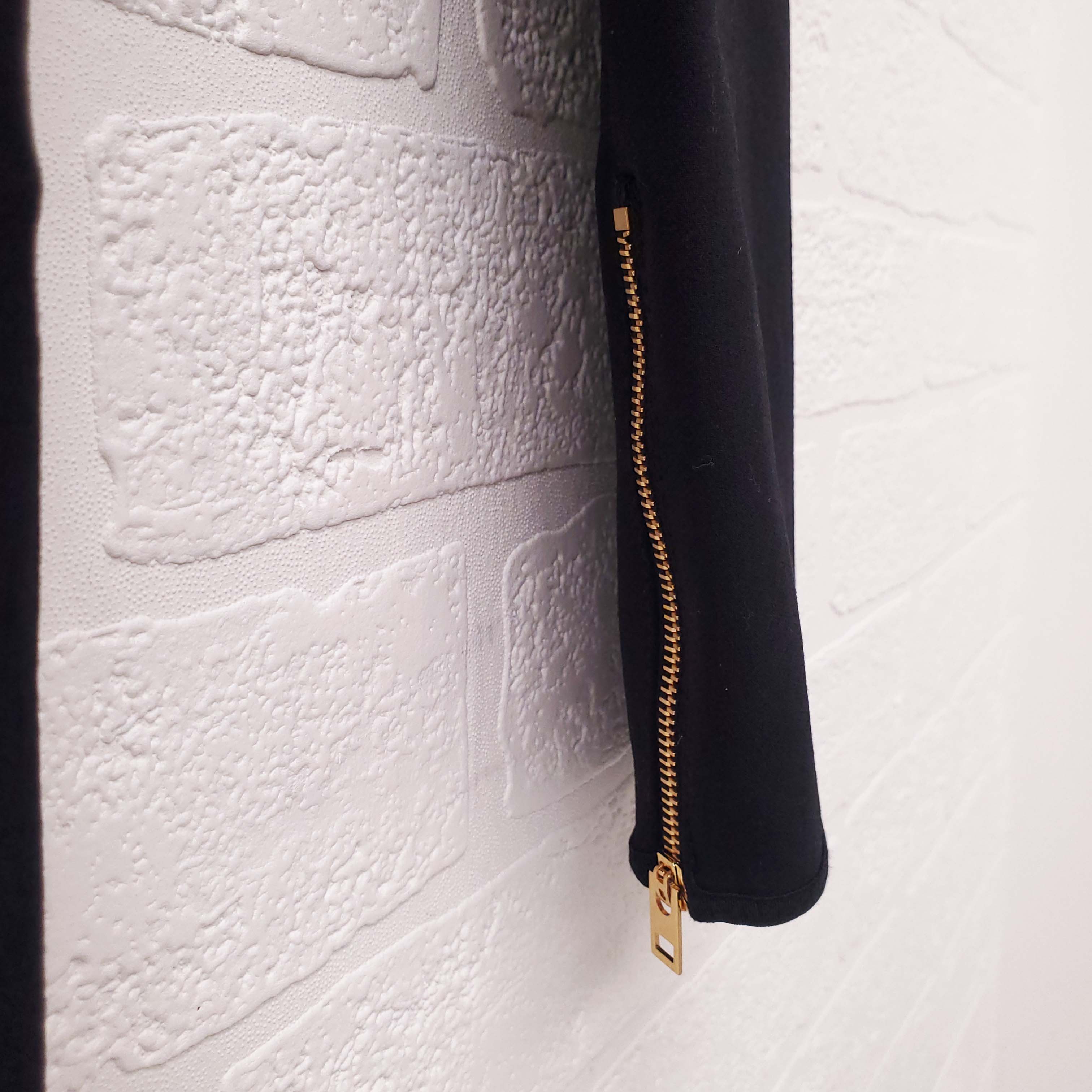 Close-up of a textured white surface with a black sleeve and gold zipper on Celine pants.